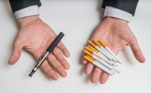 hands, palms facing up, holding cigarettes in the left hand, vaping pen in the right hand