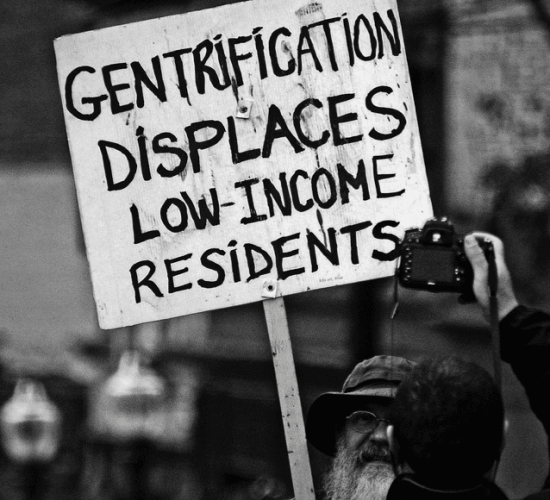 Protestor holding a sign that reads "gentrification displaces low-income residents"