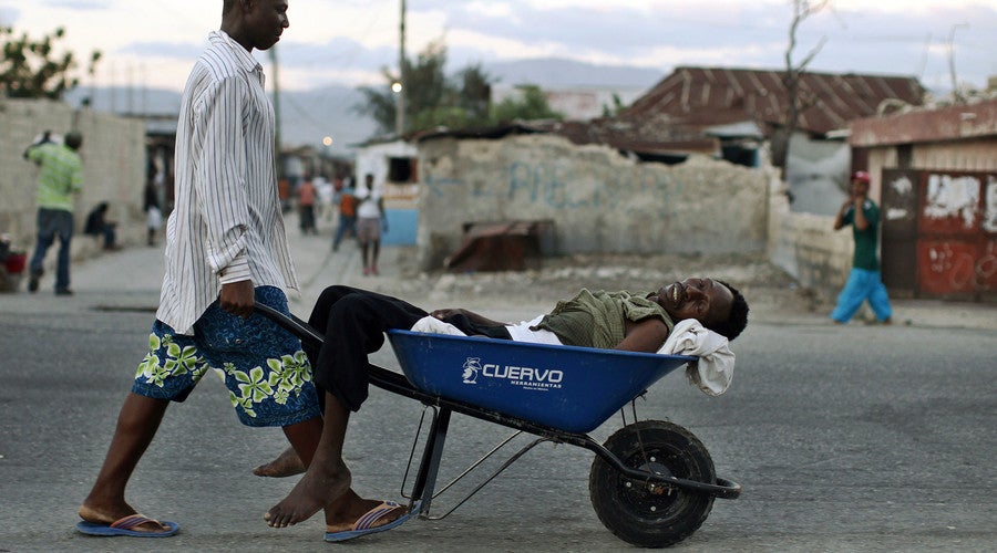 Man transporting a sick man in a wheelbarrow