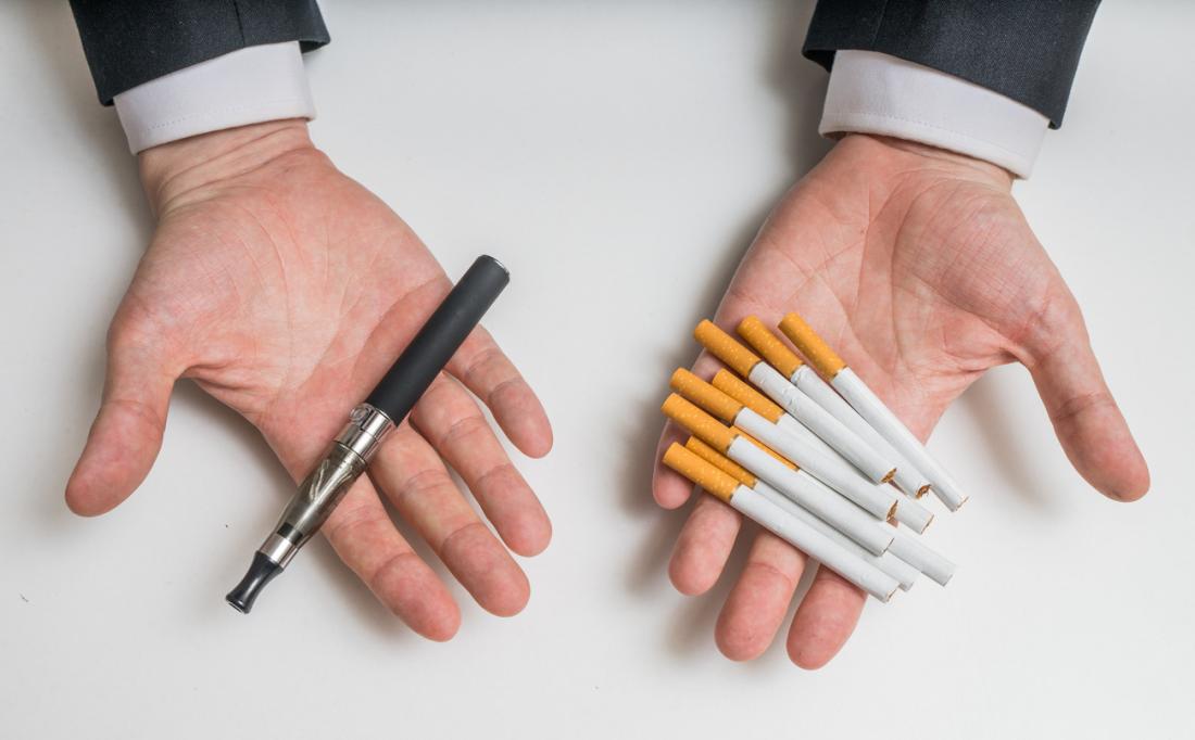 hands holding an e-cigarette and traditional cigarettes