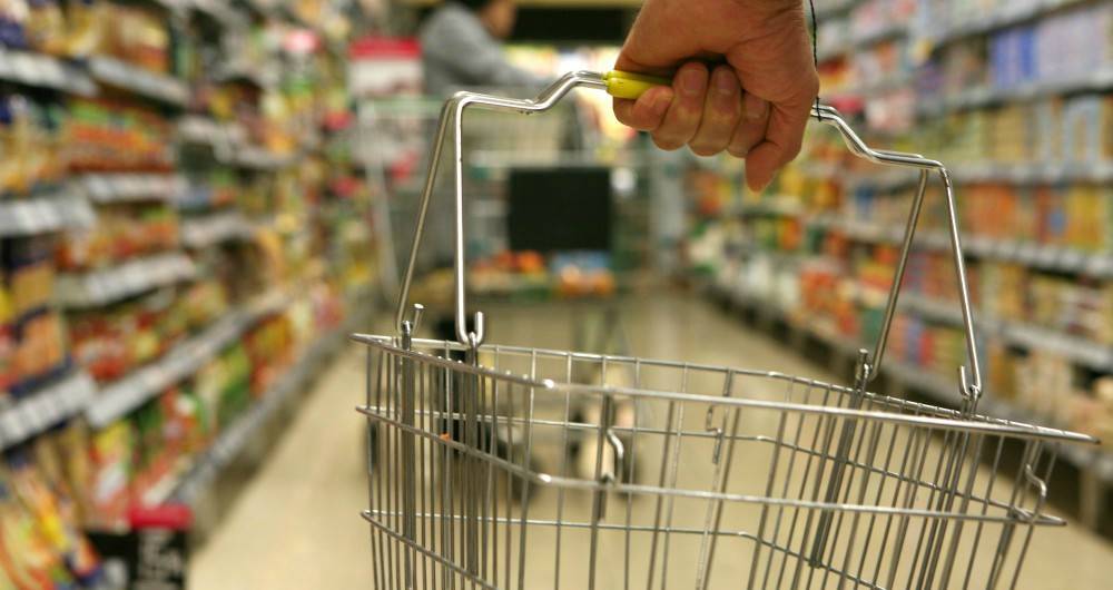 hand carrying a grocery basket in a supermarket aisle