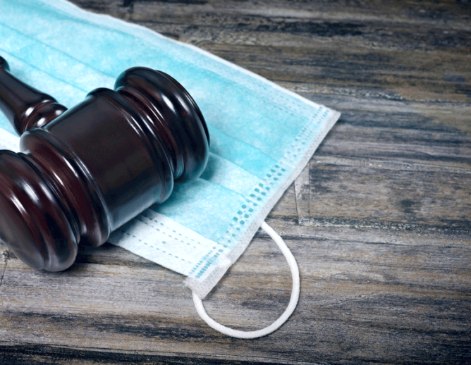 Image of gavel resting on a protective mask on a wooden table.