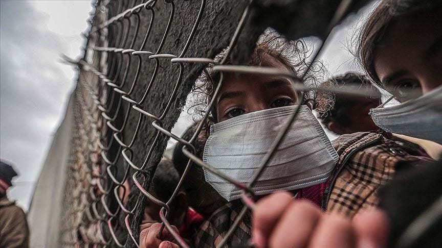 Children wearing masks and looking through a chain link fence