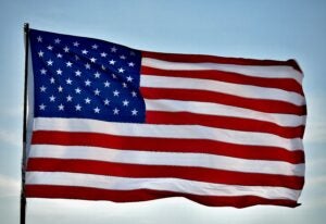 Close up US flag with blue sky and white clouds background during daytime